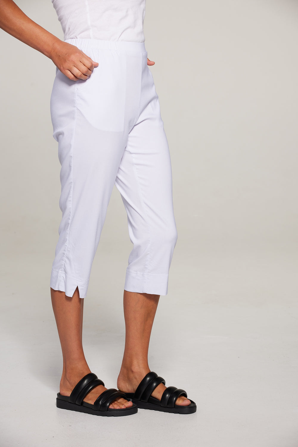 Person wearing white capri pants and black sandals on a plain background